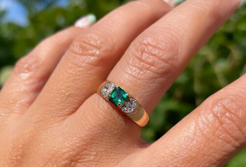 a woman's hand with a diamond and emerald ring