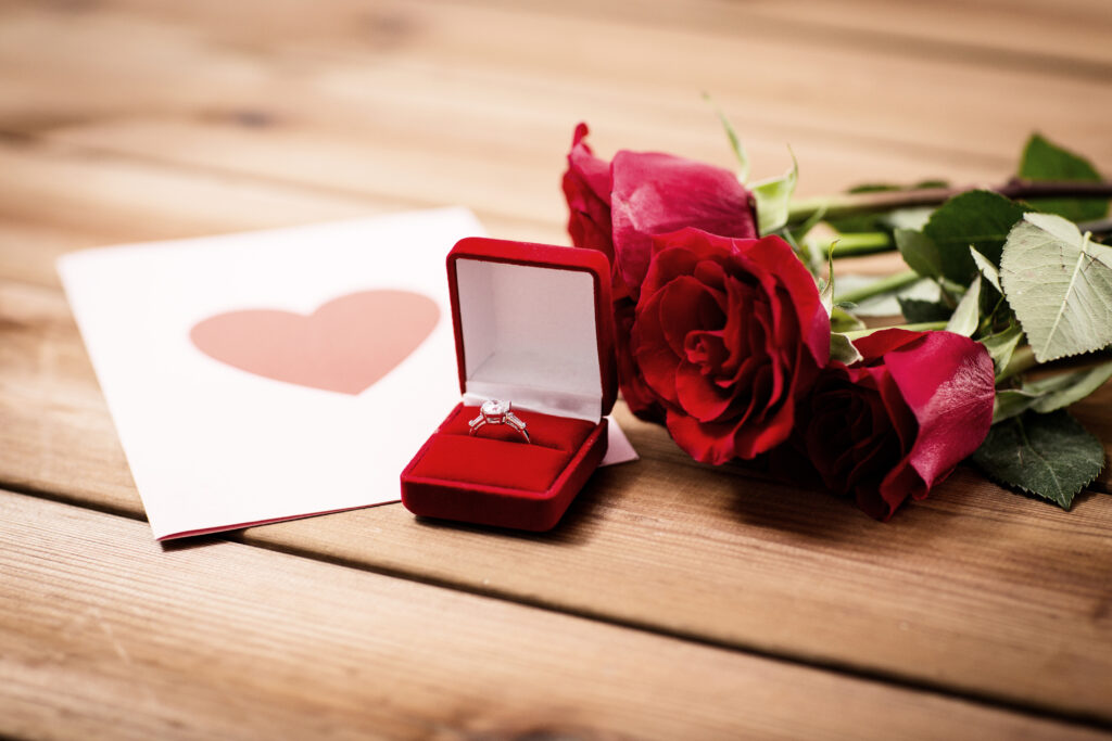 a red rose with a heart shaped ring in a box