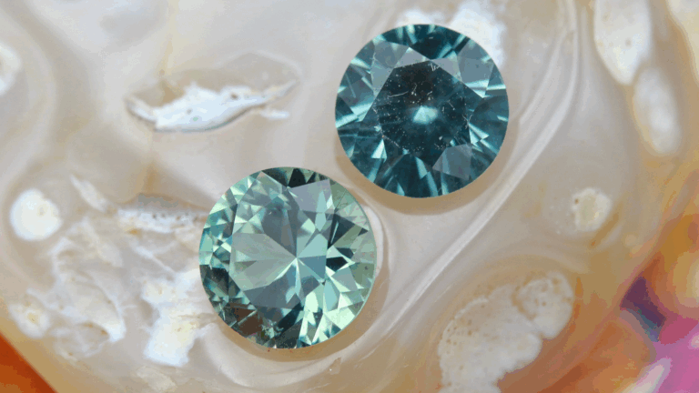 Two round faceted Montana sapphires, one a deep teal and the other a medium sea foam green, resting upon a polished rock.